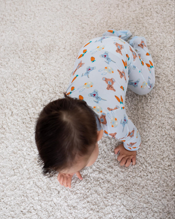A baby crawling on a textured beige carpet, wearing a light blue long-sleeve pajama set with a colorful dinosaur pattern.