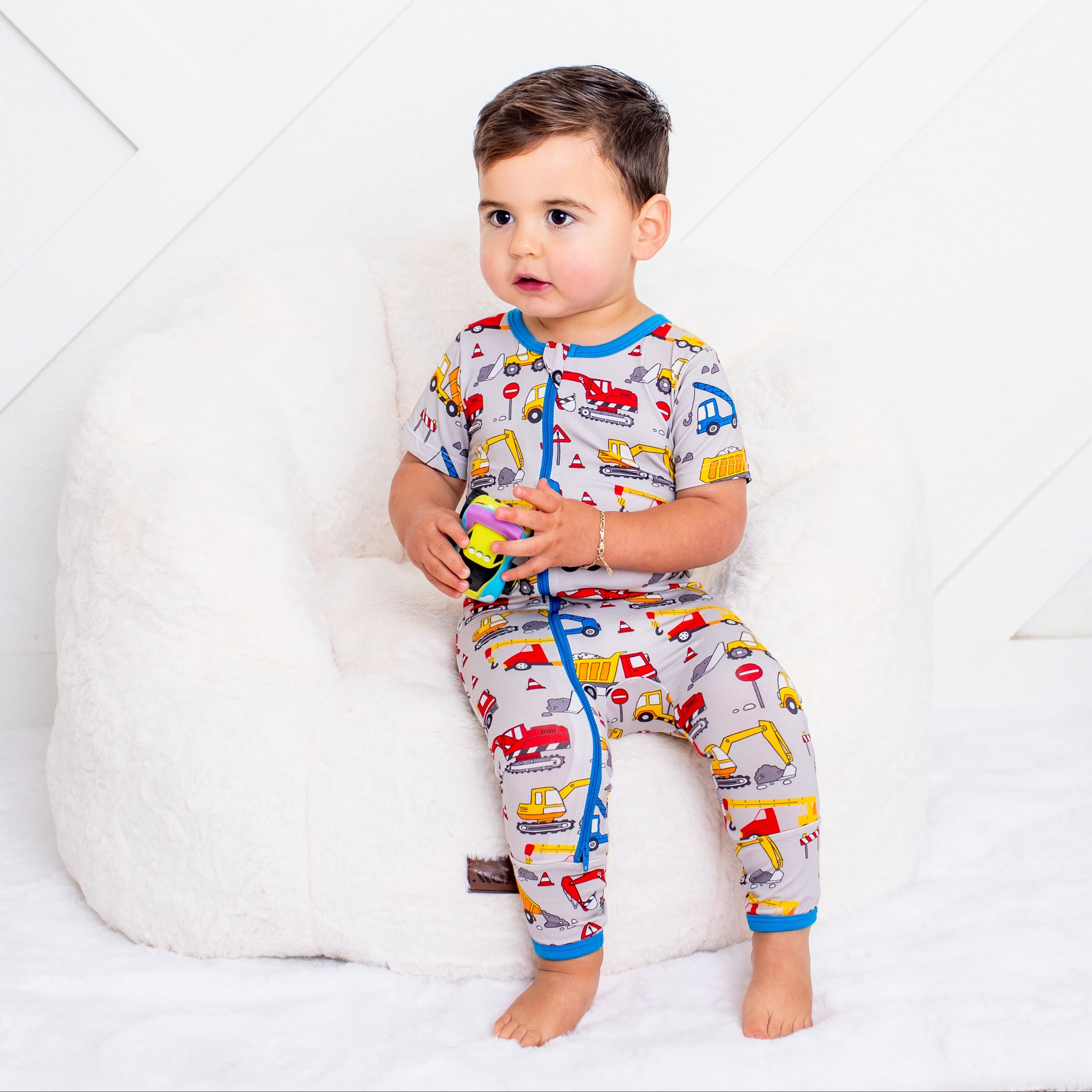 Child wearing colorful pajamas with vehicle pattern sitting on a white couch.