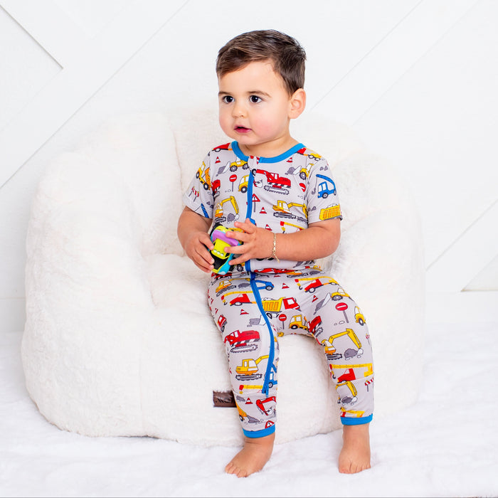Child wearing colorful pajamas with vehicle pattern sitting on a white couch.