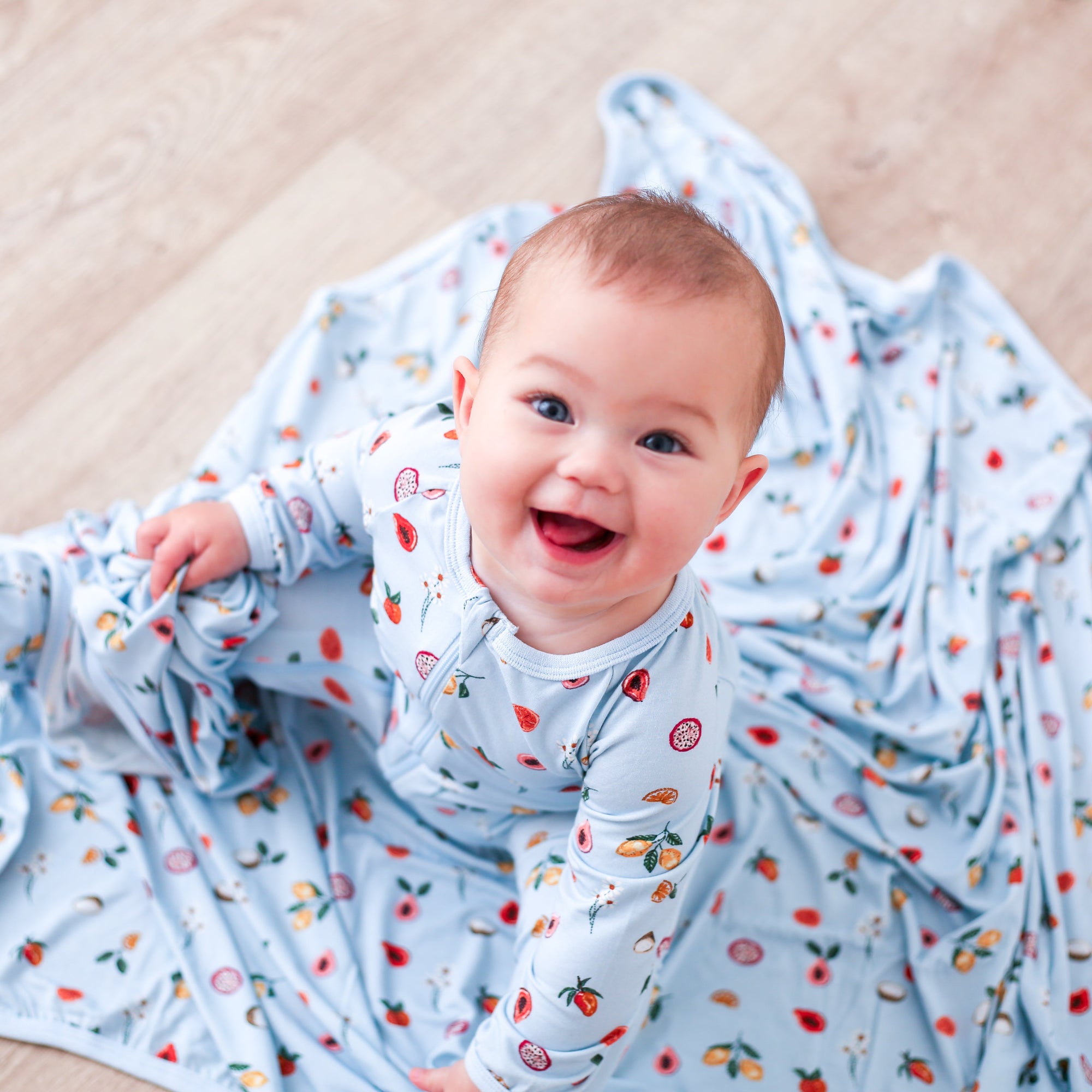 Baby lying on a wooden floor wrapped in a blue blanket with fruit pattern