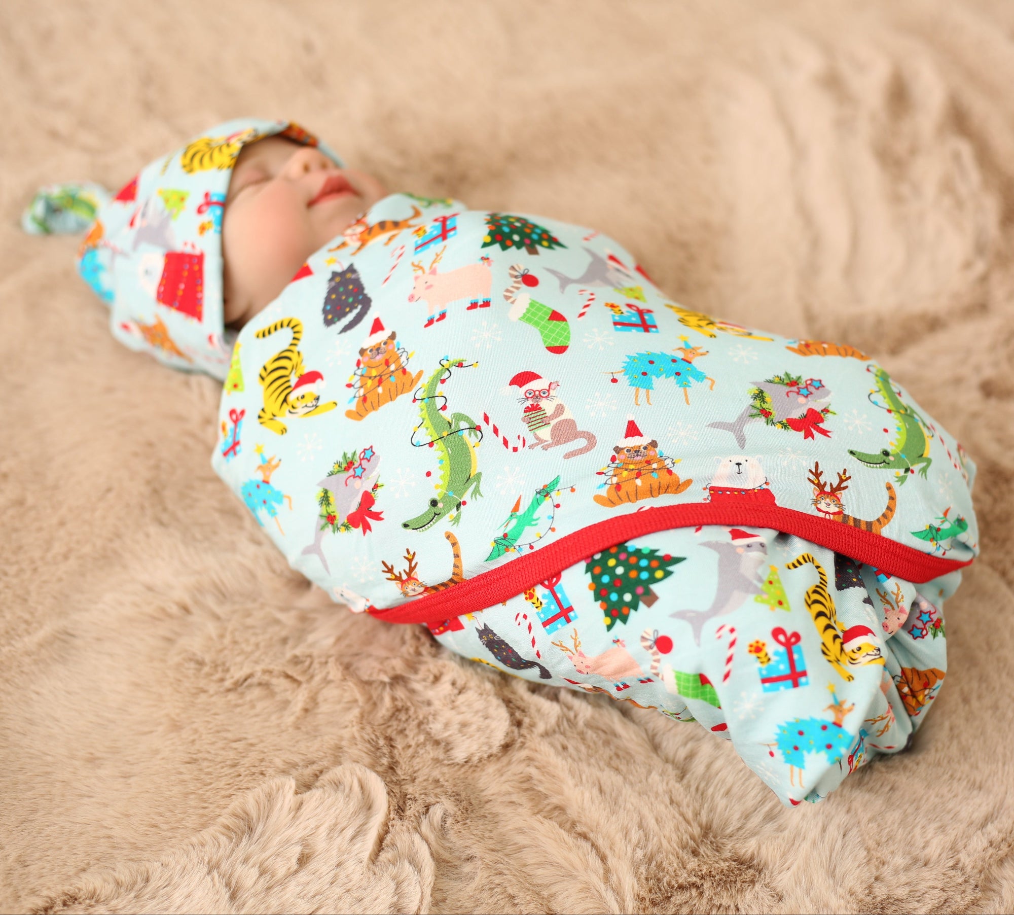 Baby swaddled in a colorful blanket with animal patterns on a sandy surface