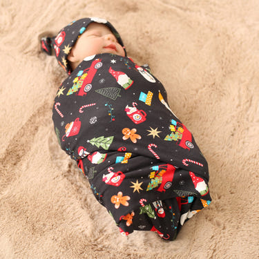 Baby swaddled in a colorful blanket with Christmas-themed patterns on sandy ground