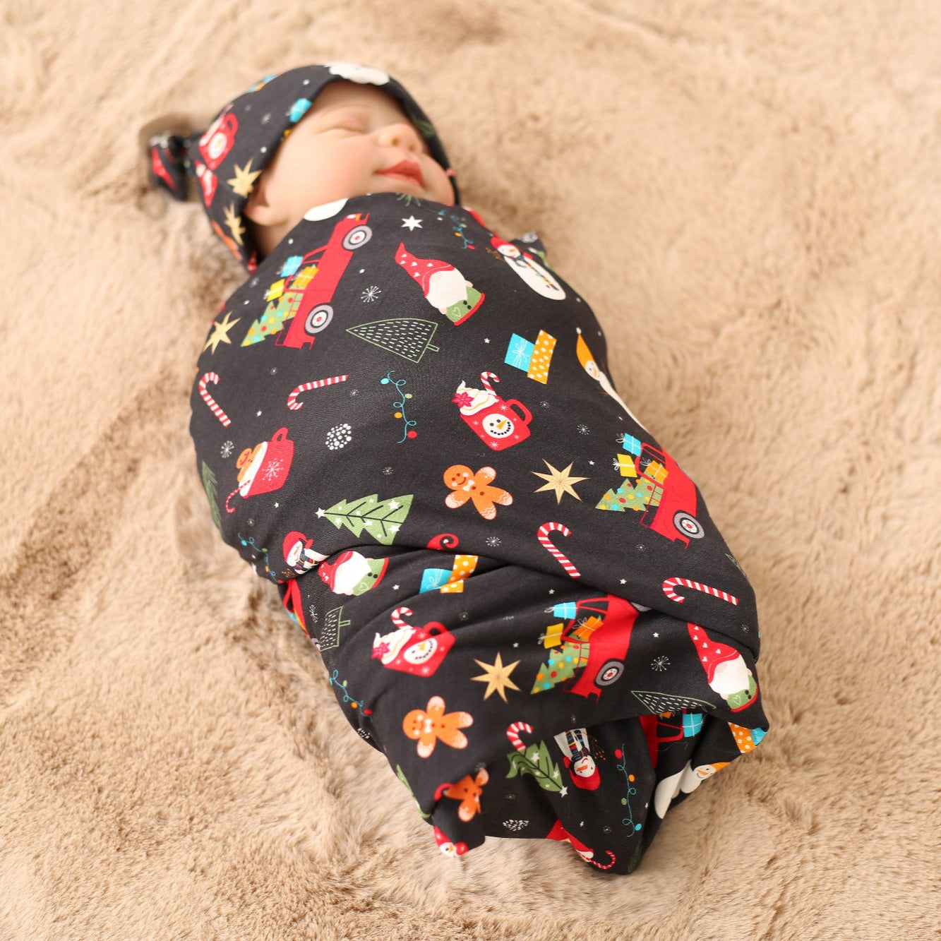 Baby swaddled in a colorful blanket with Christmas-themed patterns on sandy ground