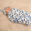 Newborn baby swaddled in a blue and black patterned blanket on a beige surface