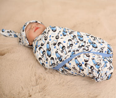 Newborn baby swaddled in a blue and black patterned blanket on a beige surface
