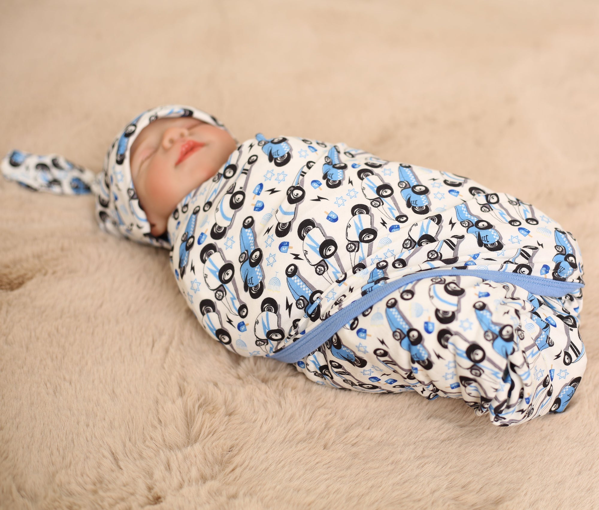 Newborn baby swaddled in a blue and black patterned blanket on a beige surface