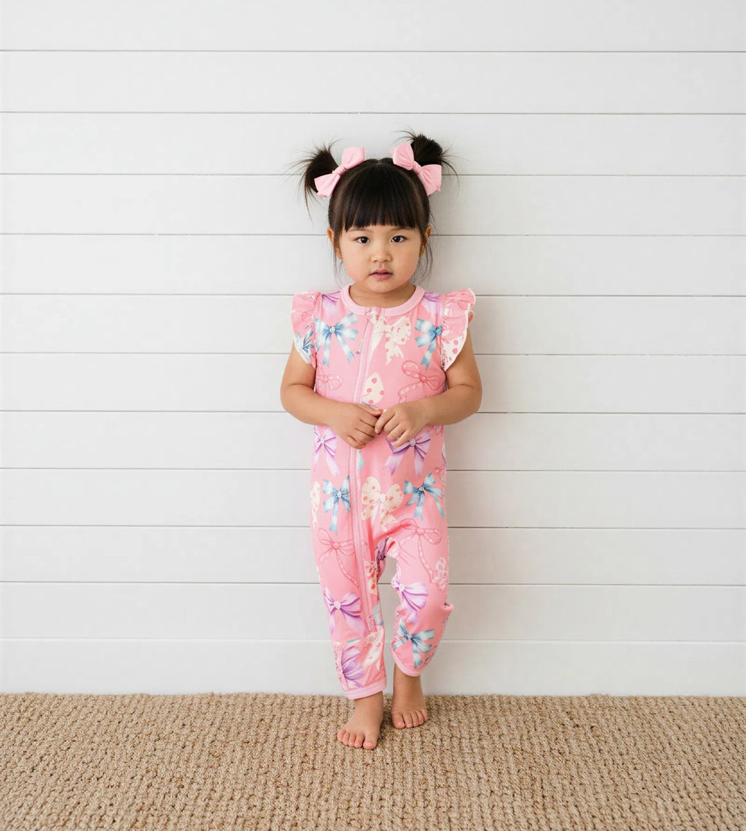 Young girl in a pink floral outfit standing against a white wooden panel background