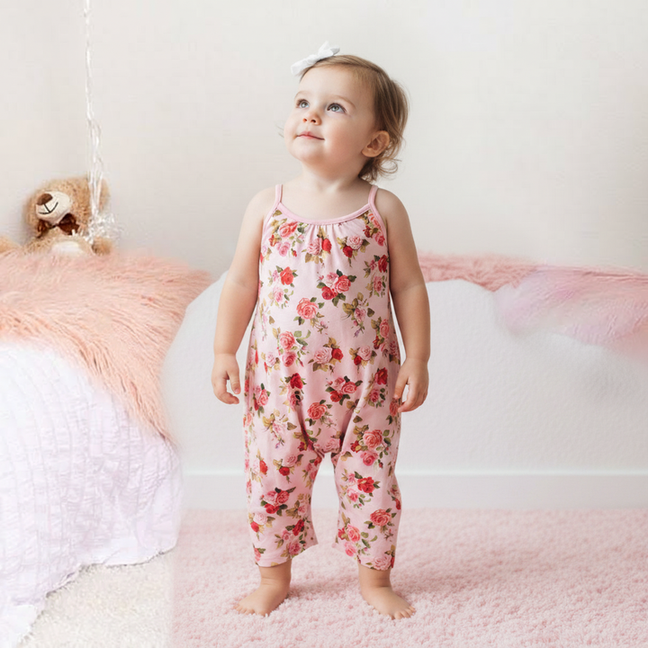 Child wearing a floral pink romper standing in a softly blurred room.
