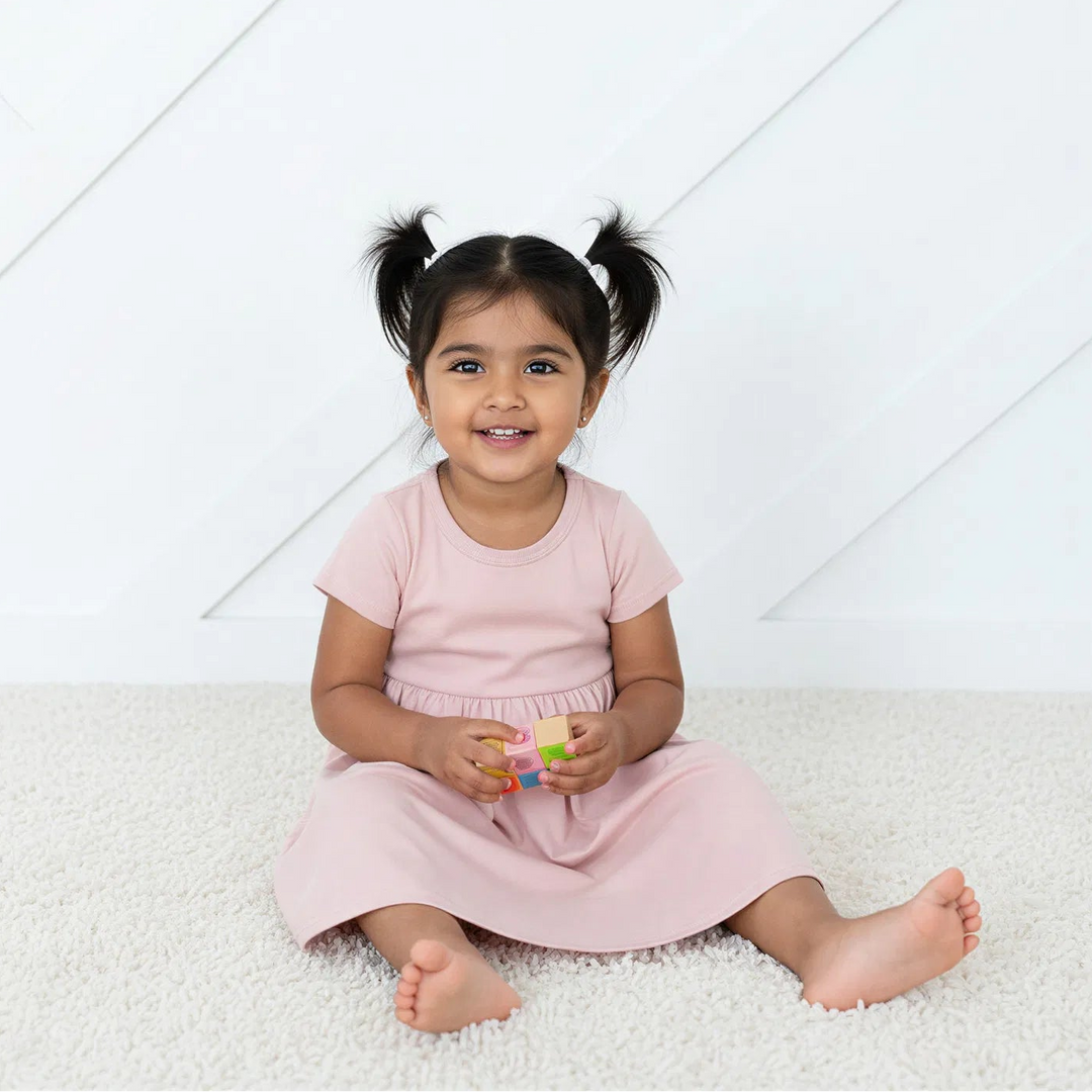 Young girl in a pink dress sitting on a white carpet