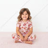 Young girl wearing pink floral pajamas sitting on a white surface.