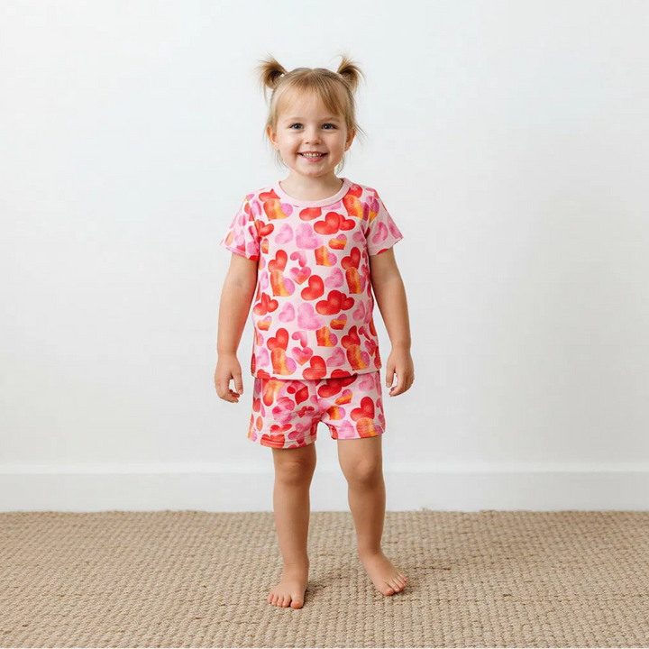 Young girl wearing a pink floral outfit standing on a beige carpet with a white wall background