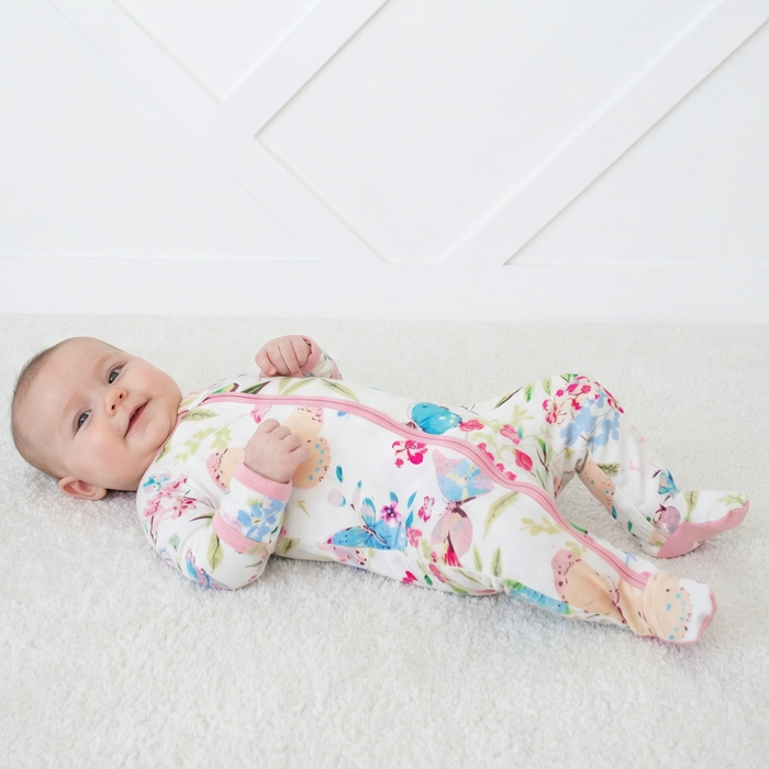 Baby lying on a white blanket wearing a colorful floral outfit with zippers.
