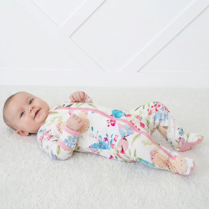 Baby lying on a white blanket wearing a colorful floral outfit with zippers.