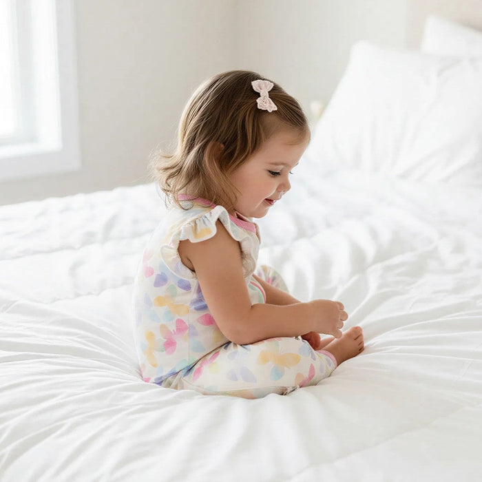 Child wearing a colorful outfit sitting on a white bed