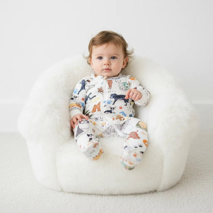 Baby wearing a onesie with animal prints sitting on a white cushion.