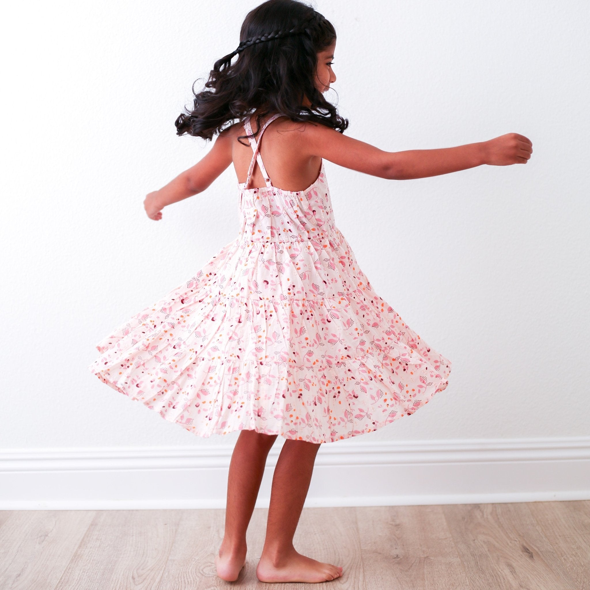 Young girl in a floral dress twirling against a white wall.