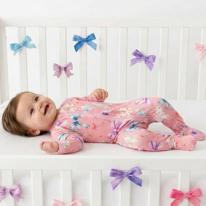 Baby lying on a crib wearing a pink floral onesie with colorful bows.