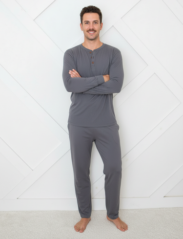 Man wearing gray long-sleeve top and pants standing against a white geometric-patterned wall.
