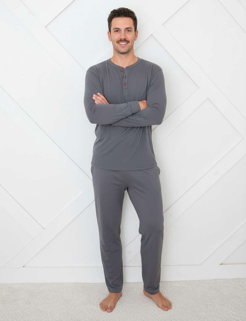 Man wearing gray long-sleeve top and pants standing against a white geometric-patterned wall.