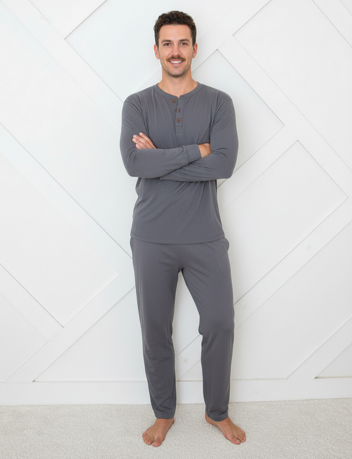 Man wearing gray long-sleeve top and pants standing against a white geometric-patterned wall.