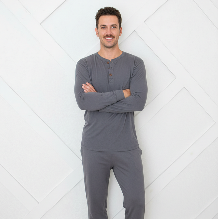 Man wearing gray pajamas standing against a white geometric-patterned wall.
