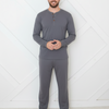 Man wearing gray long-sleeve top and pants standing against a white geometric-patterned wall.