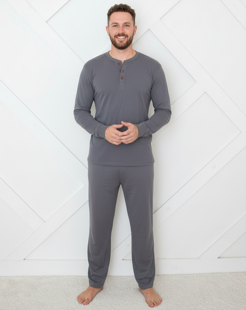 Man wearing gray long-sleeve top and pants standing against a white geometric-patterned wall.