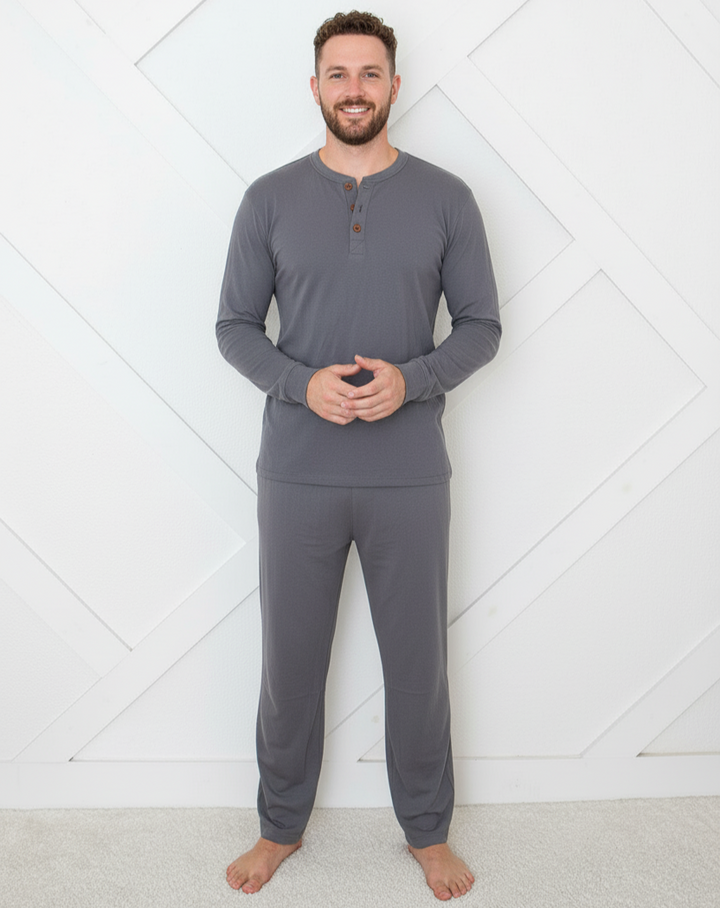 Man wearing gray long-sleeve top and pants standing against a white geometric-patterned wall.